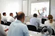 Instructor giving a technical presentation to a classroom of participants, with industrial equipment diagrams displayed on a screen.